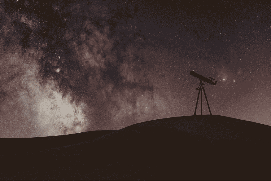 Telescópio sob céu estrelado e Via Láctea, instrumento essencial para observar regiões do espaço estudadas pela astrobiologia.