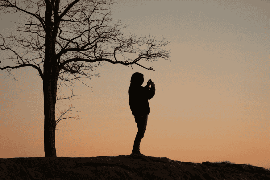 Silhueta de pessoa fotografando com celular ao pôr do sol, referência para iniciantes aprenderem composição e estabilidade na astrofotografia.