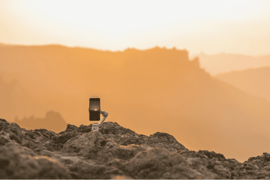 Smartphone apoiado em pequeno tripé sobre terreno rochoso, mostrando uma configuração prática para astrofotografia com celular.