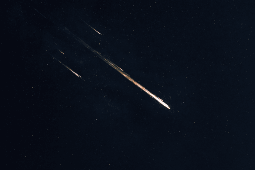 Vários meteoros com rastros luminosos atravessando o céu escuro, representando o pico da chuva de meteoros Gemínidas.