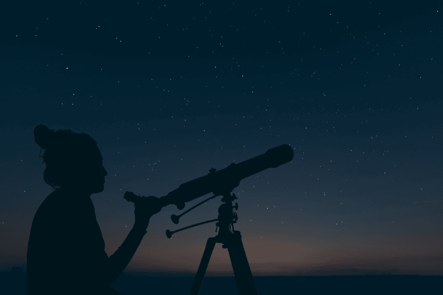 Pessoa observando o céu noturno com telescópio durante a visualização de estrelas e constelações