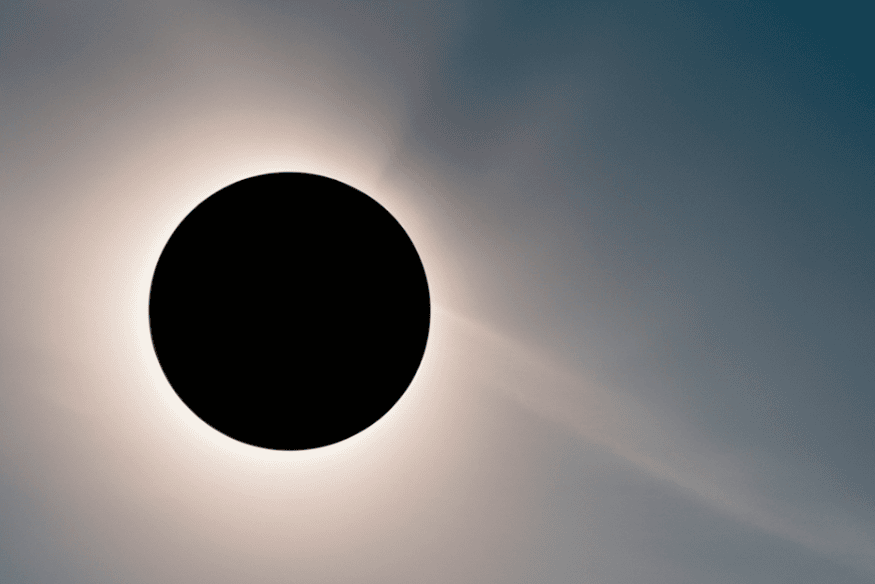 Eclipse solar total com disco escuro central e coroa solar esbranquiçada ao redor, em céu com gradiente.