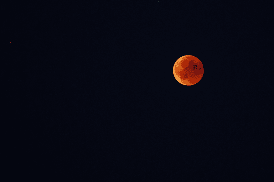 Lua avermelhada em fundo escuro, registro de eclipse lunar total com tonalidade vermelha causada pela atmosfera terrestre.