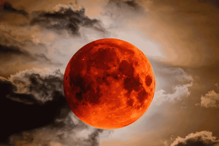 Close da Lua vermelha em eclipse lunar total com nuvens ao redor, destacando a coloração avermelhada do disco lunar.