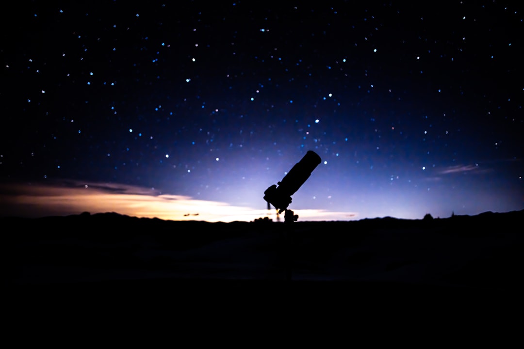Astrônomo amador com telescópio em campo aberto sob céu estrelado